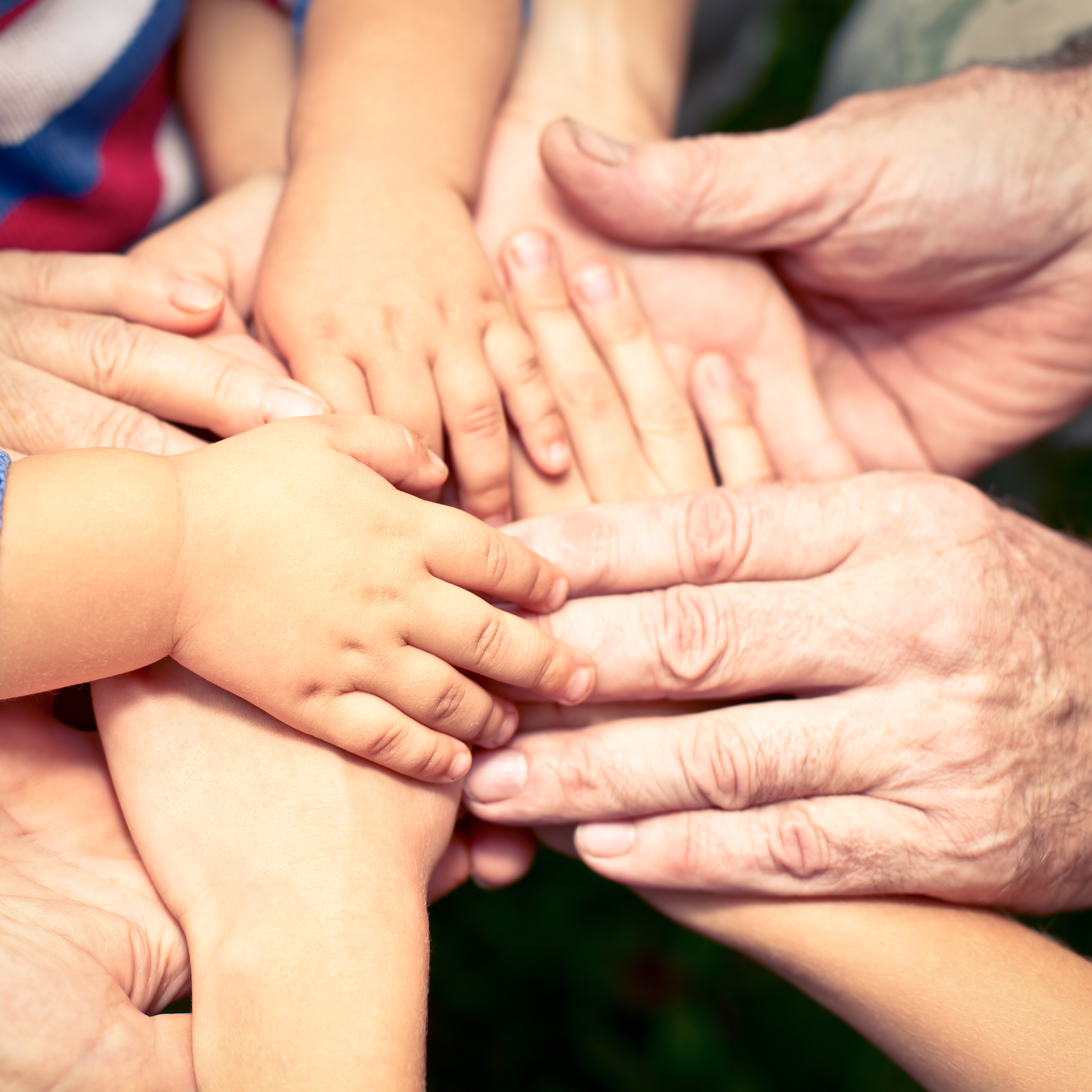 Many hand placed over one another. The hands clearly belong to people of different ages, from children to the elderly.